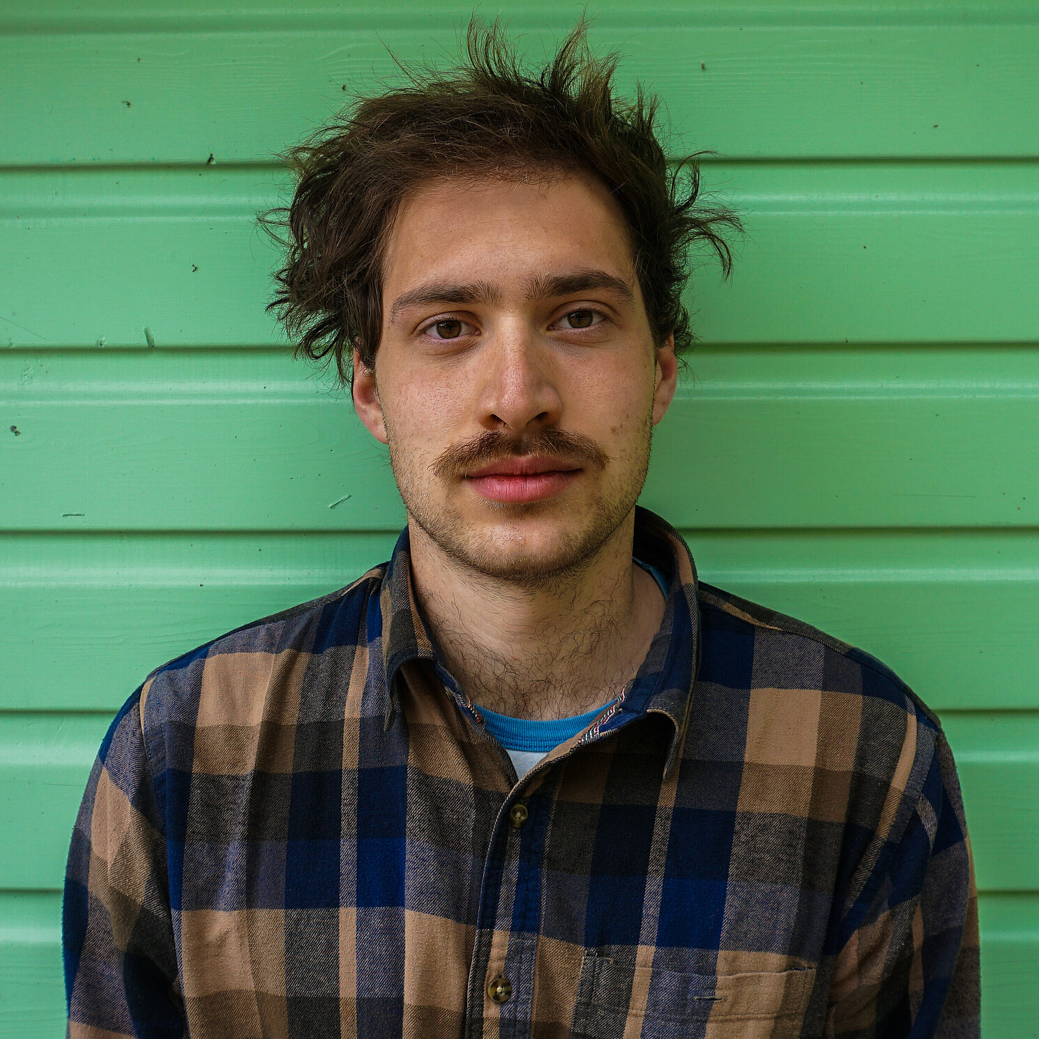 Auf dem Foto ist eine Person frontal zu sehen. Sie steht vor einem grünen Hintergrund.