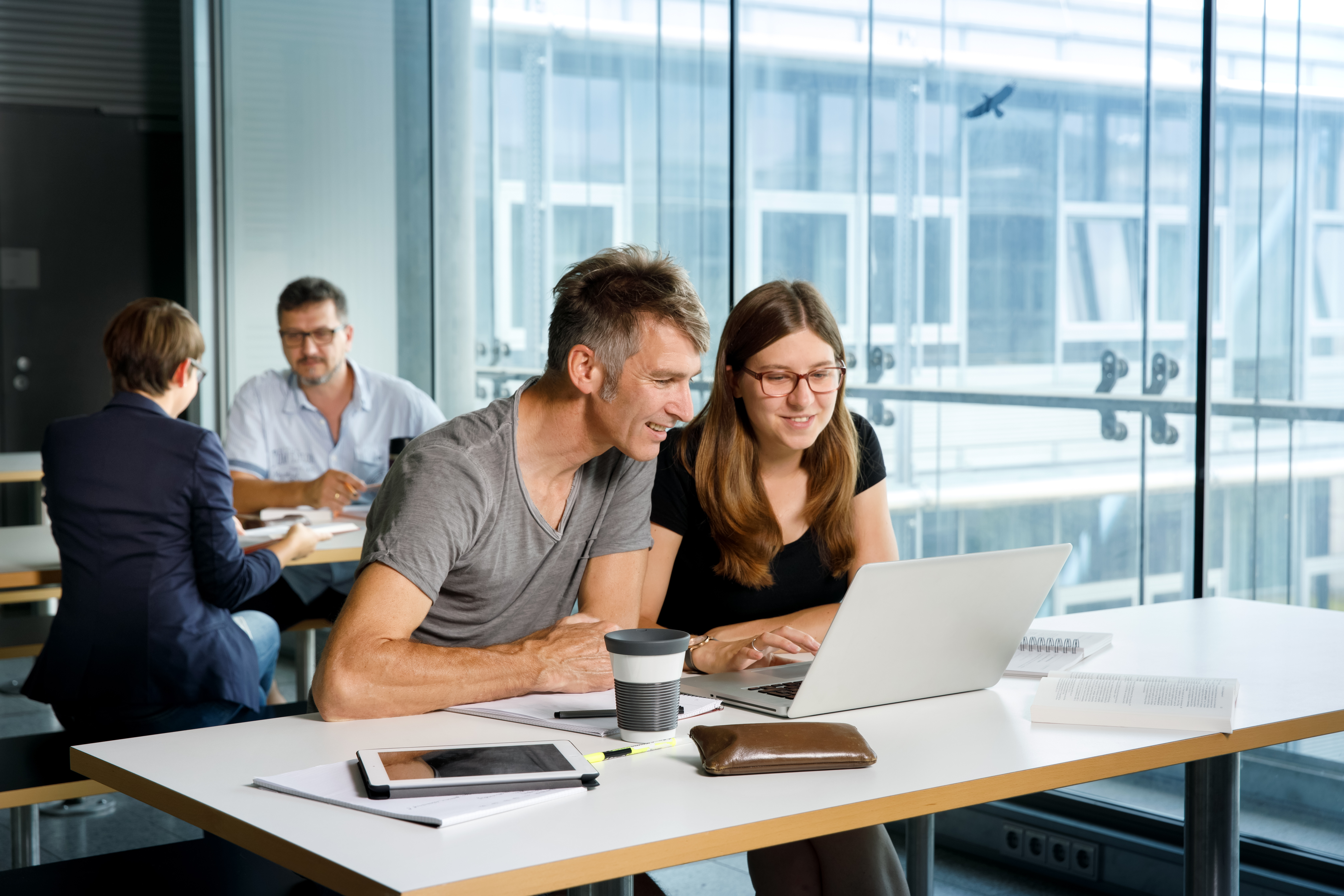 Vier Studierende lernen und arbeiten an ihren Tischen mit Büchern und Laptops