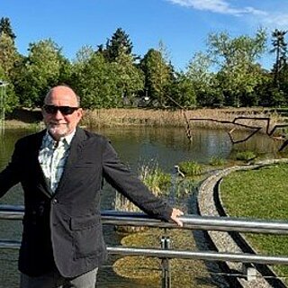 Ein Mann steht an einem Geländer mit einem Teich im Hintergrund.