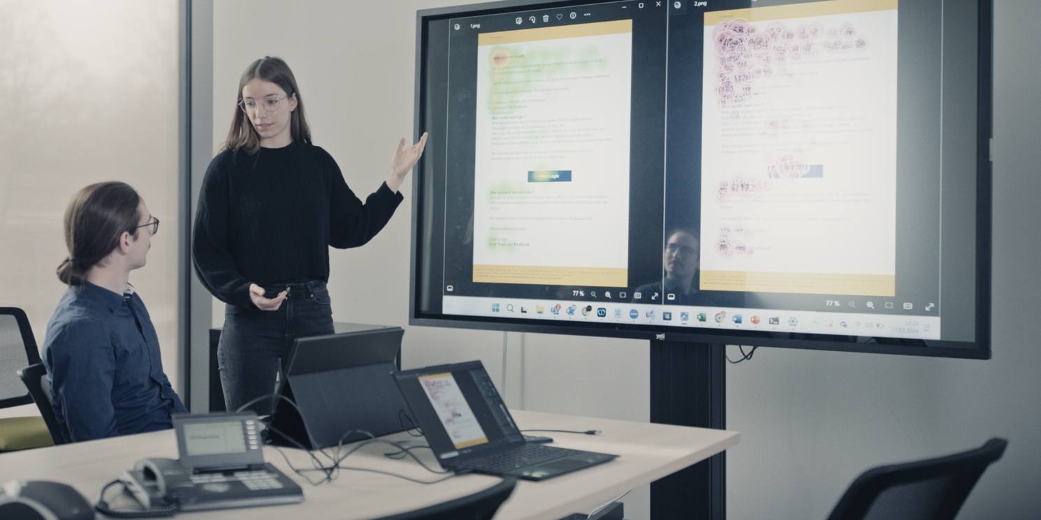 Meret Kristen und Fabian Engl stehen in einem Seminarraum an der OTH Regensburg und werten gemeinsam Daten vor einer großen Leinwand aus. Links und rechts ist eine Heatmap zusehen, die farbige Flecken aufweist und so Informationen übermittelt.
