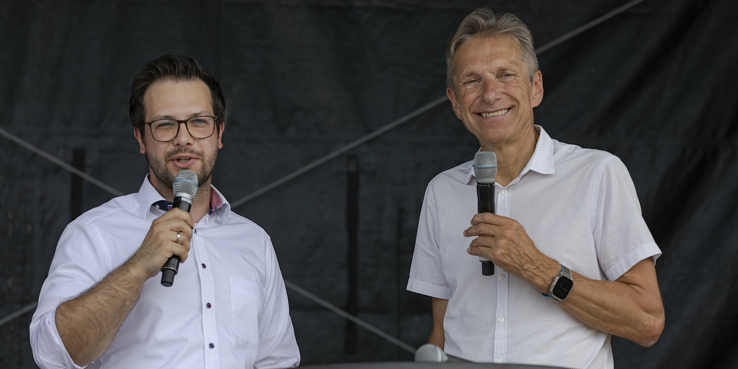 Zwei Männer stehen nebeneinander, jeder hält ein Mikrofon in der Hand.