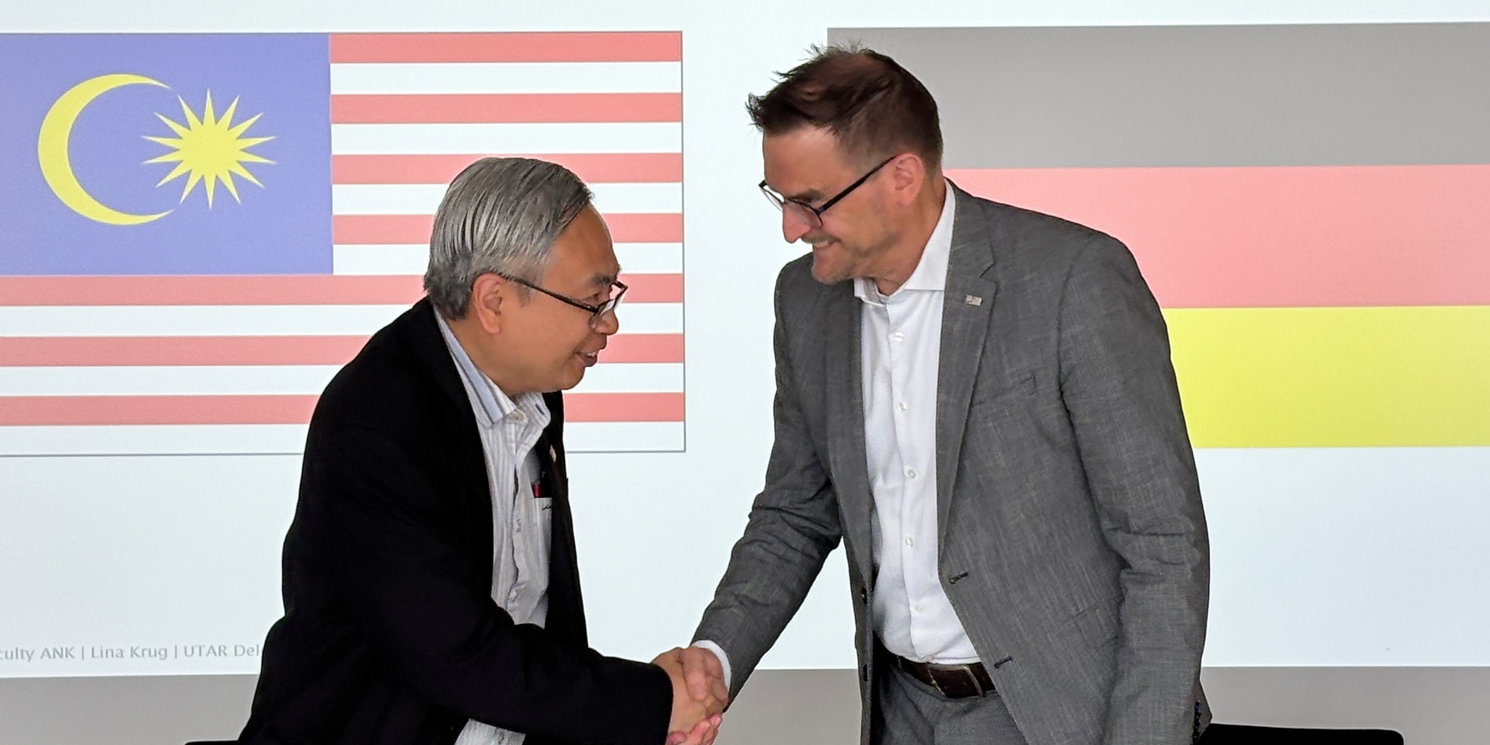 UTAR-Präsident Ir. Professor Dato' Dr. Ewe Hong Tat (l.) und Prof. Dr. Oliver Steffens geben sich die Hände nach der Vertragsunterzeichnung. Hintergrund: Flaggen von Malaysia und Deutschland