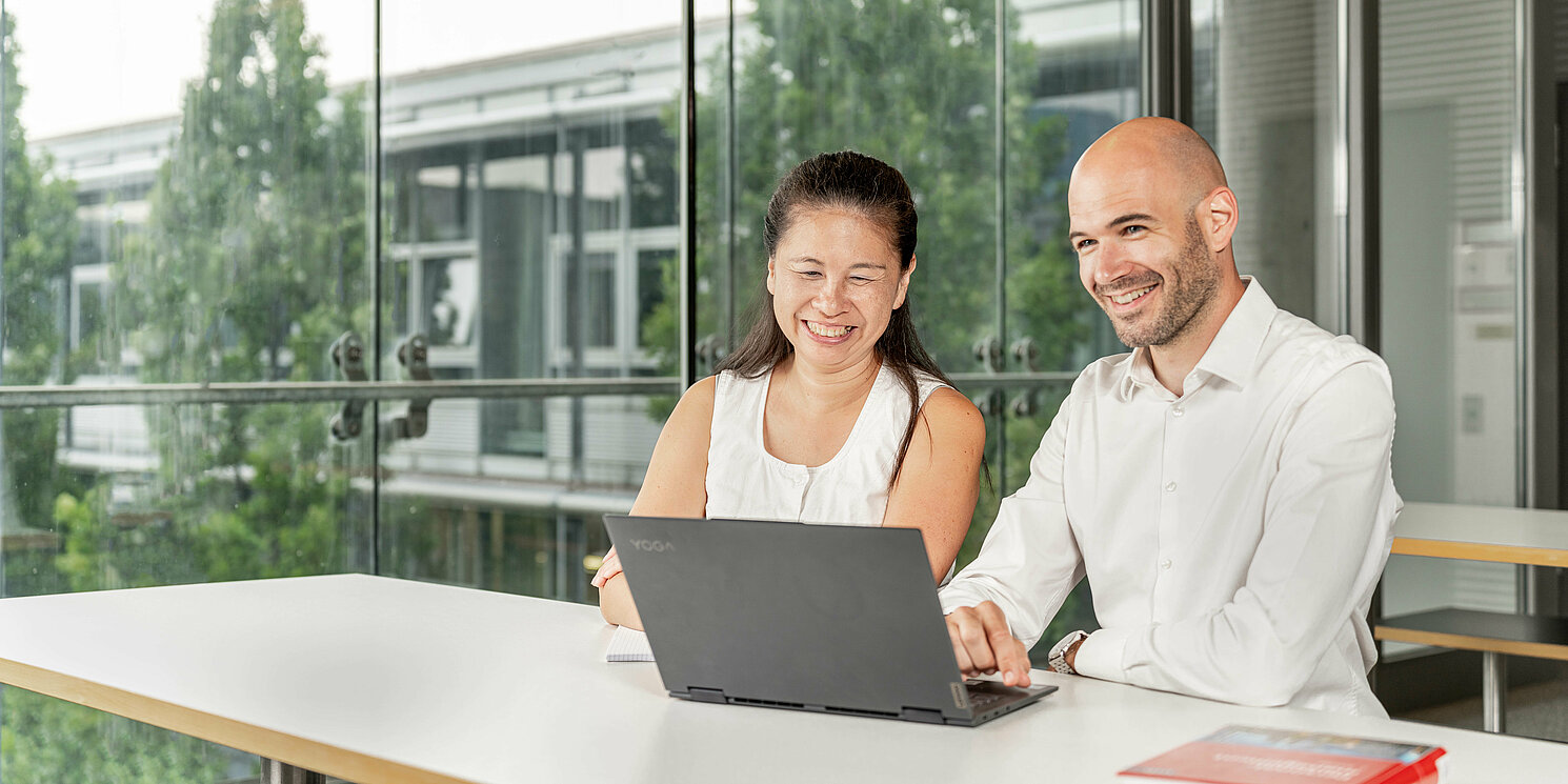 Zwei Studierende lernen gemeinsam an einem Tisch mit einem Laptop. 