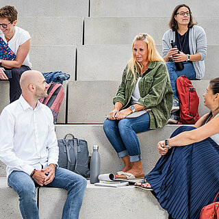 Mehrere Studierende sitzen mit ihren Lernmaterialien auf einer großen Treppe.