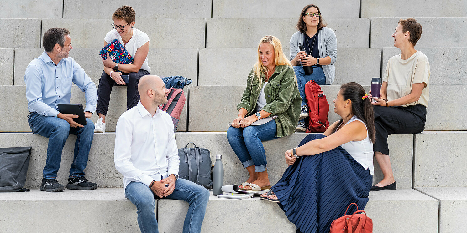 Mehrere Studierende sitzen mit ihren Lernmaterialien auf einer großen Treppe.