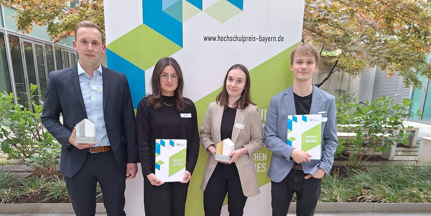 Vier Personen mit Auszeichnung vor einem Plakat.