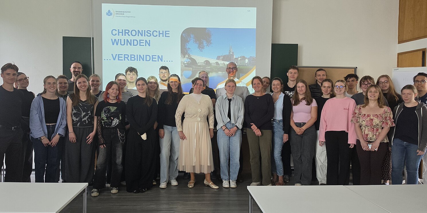 Ein Gruppenfoto mit allen Teilnehmenden des Seminar, vor einer Leinwand, welche die Folie zeigt "Chronische Wunden...verbinden..."