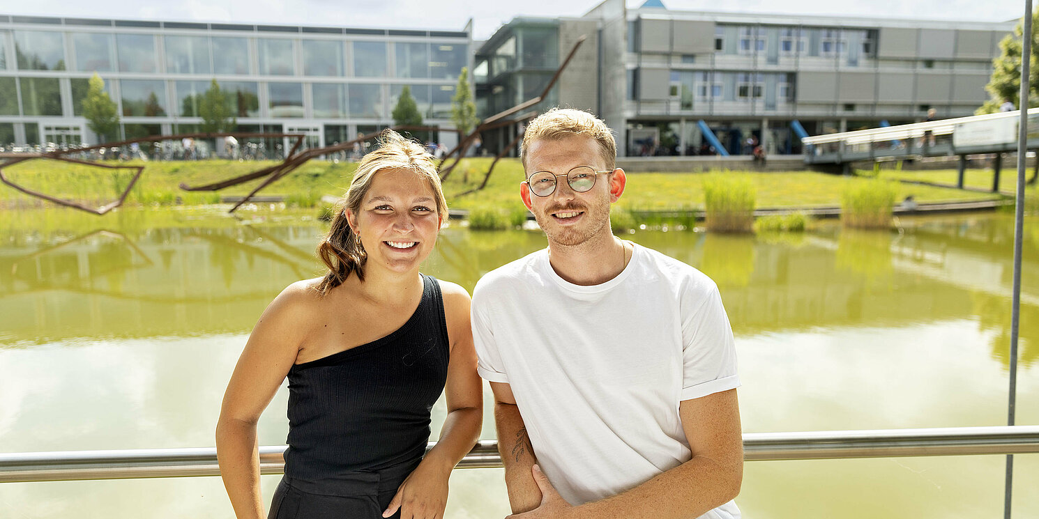 Zwei Personen, die an einem Geländer lehen. Im Hintergrund ein See und das OTH Gebäude.