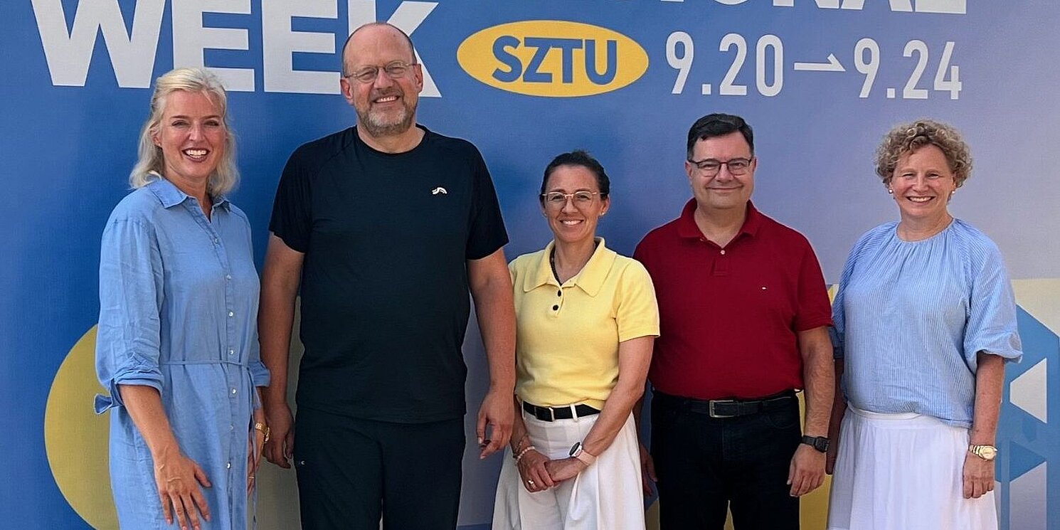 Ein Gruppenfoto vor einem großen Plakat als Hintergrund mit dem Motto der International Week.