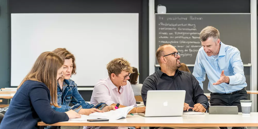 Studierende und ihr Dozent arbeiten in einem Seminarraum.