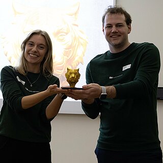 Eine Frau und ein Mann heben gemeinsam die Siegertrophäe