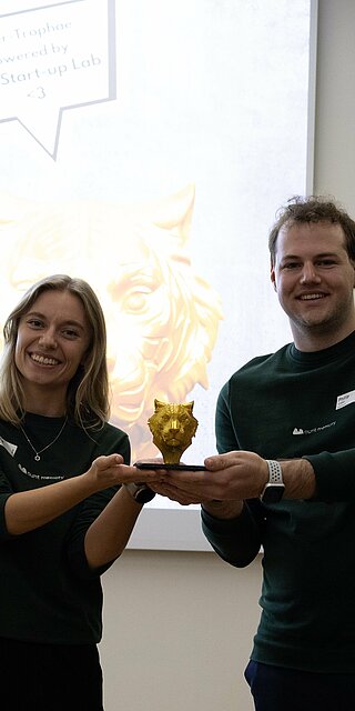 Eine Frau und ein Mann heben gemeinsam die Siegertrophäe