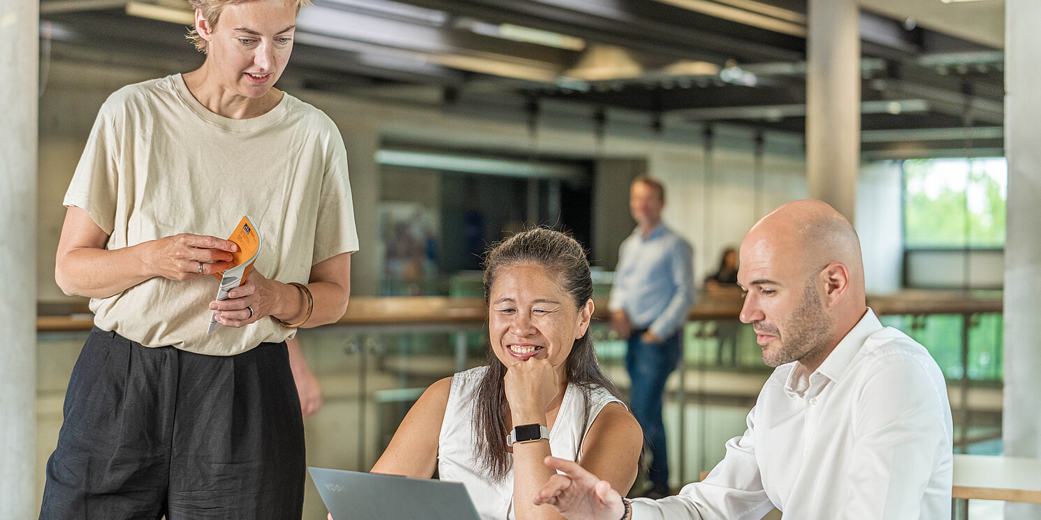 Business Administration – General Management berufsbegleitend studieren Drei Studierende tauschen sich über einem Laptop aus.
