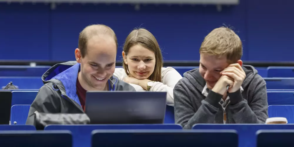 Drei junge Menschen gucken in einen Laptop