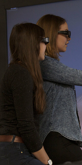 Zwei Frauen mit VR-Brillen deuten auf ein Projektbild.