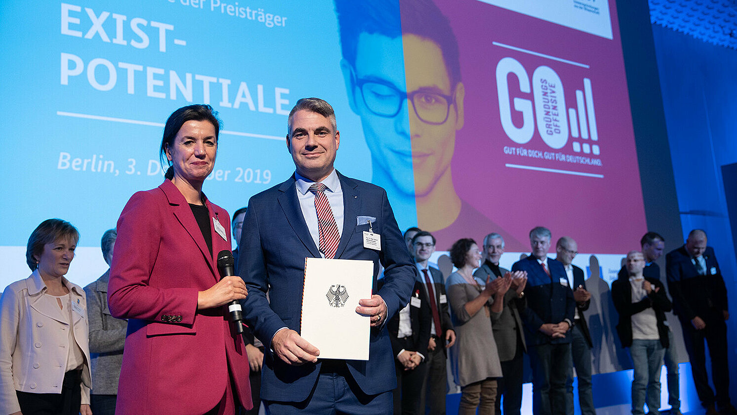 Dr. Sabine Hepperle vom Bundesministerium für Wirtschaft und Energie übergibt die Urkunde an den Sprecher des Verbundprojektes, Prof. Dr. Sean Patrick Saßmannshausen, OTH Regensburg.