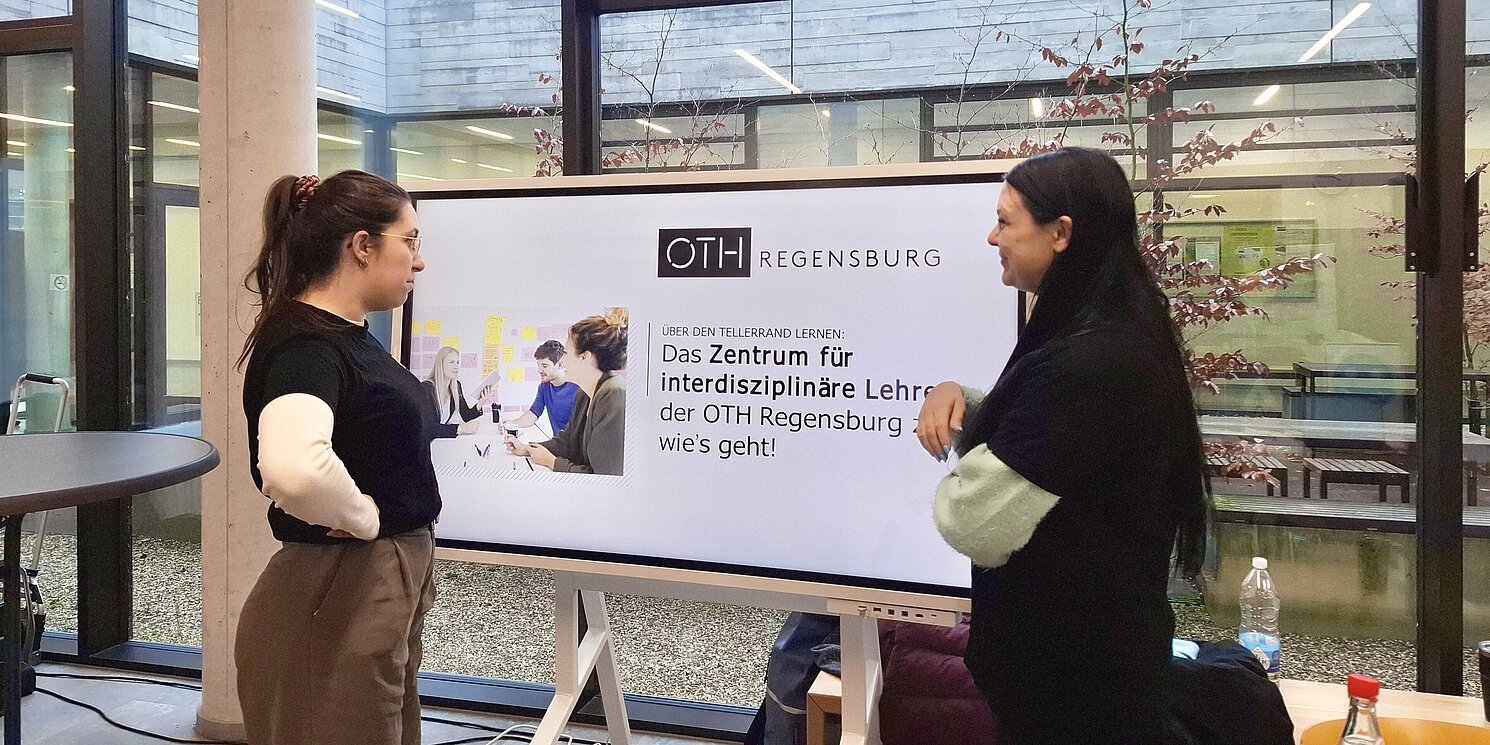 Zwei Kolleginnen der OTH Regensburg stehen vor einem digitalen Flipchart und präsentieren die wesentlichen Punkte des Zentrums für interdisziplinäre Lehre.