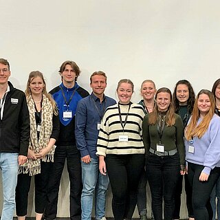 Gruppenbild mit 16 Personen vor einer Wand