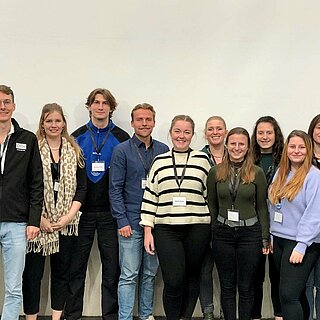 Gruppenbild mit 16 Personen vor einer Wand