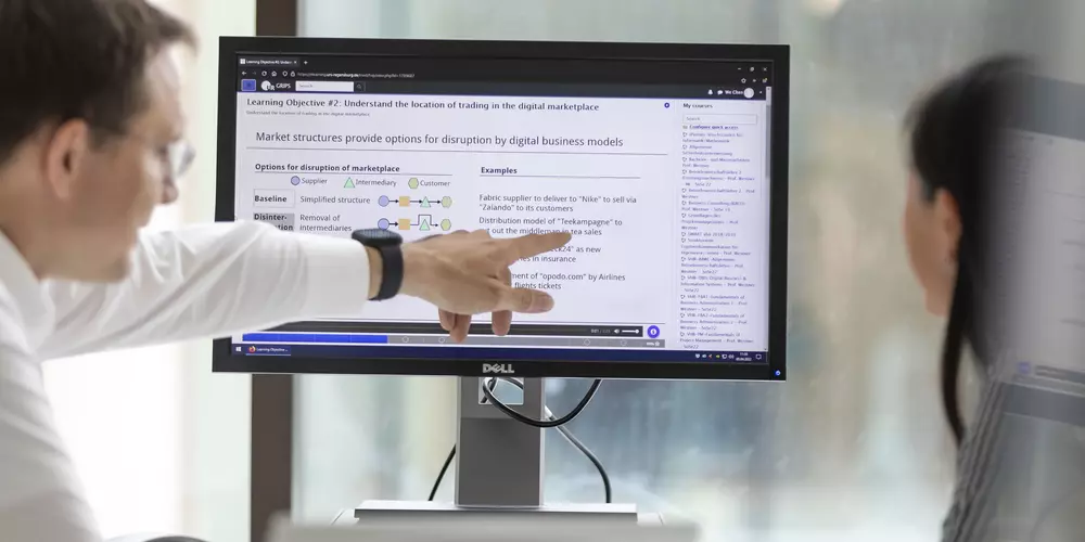 A man in a white shirt points to a screen and explains something to a young employee.