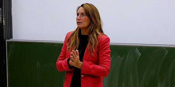 A woman in a red blazer stands in a lecture hall.