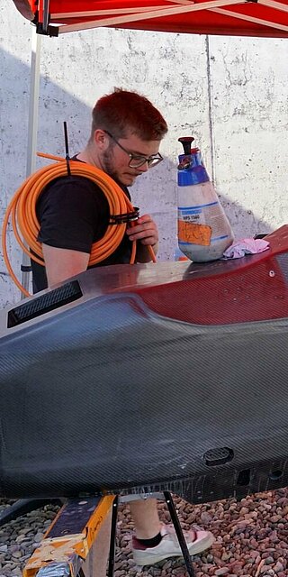Auf dem Bild ist der Prototyp des neuen Rennwagens der Formular Students 2026 zu sehen. Zwei Mitglieder arbeiten an der Schale des Rennwagens