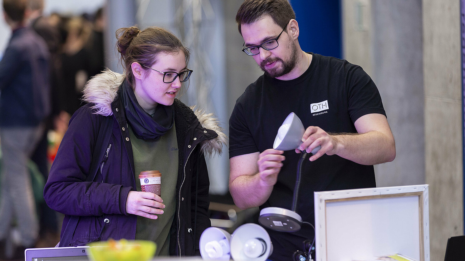 Ein Mitarbeiter der Fakultät Elektro- und Informationstechnik der OTH Regensburg zeigt einer Besucherin verschiedene Leuchtmittel-Technologien und erläutert die unterschiedlichen Farbspektra.