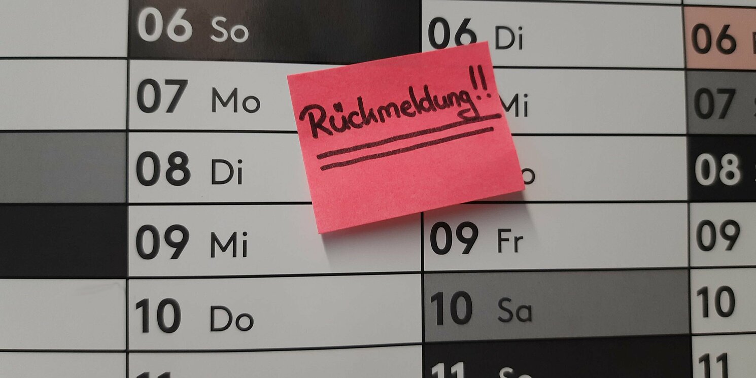 Wandkalender mit einem Notizzettel der an die Rückmeldung erinnert.