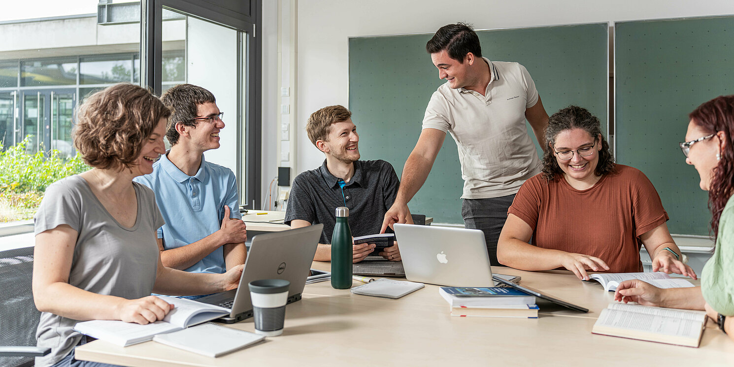 Hochschulzertifikat Betriebliches Gesundheitsmanagement berufsbegleitend absolvieren Studierende arbeiten in einer Lerngruppe mit Laptops und Unterlagen an einem großen Tisch.