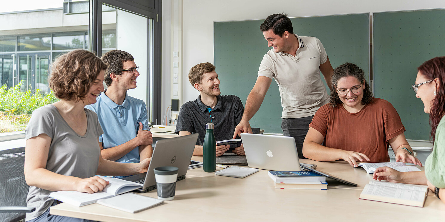 Studierende arbeiten in einer Lerngruppe mit Laptops und Unterlagen an einem großen Tisch.