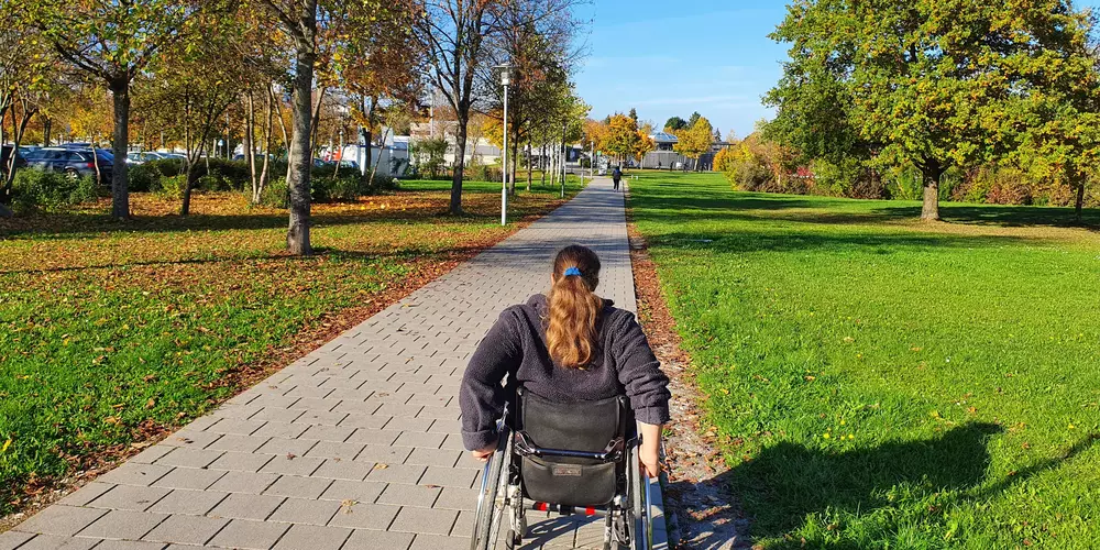 Eine Rollstuhlfahrerin fährt einen Weg entlang.