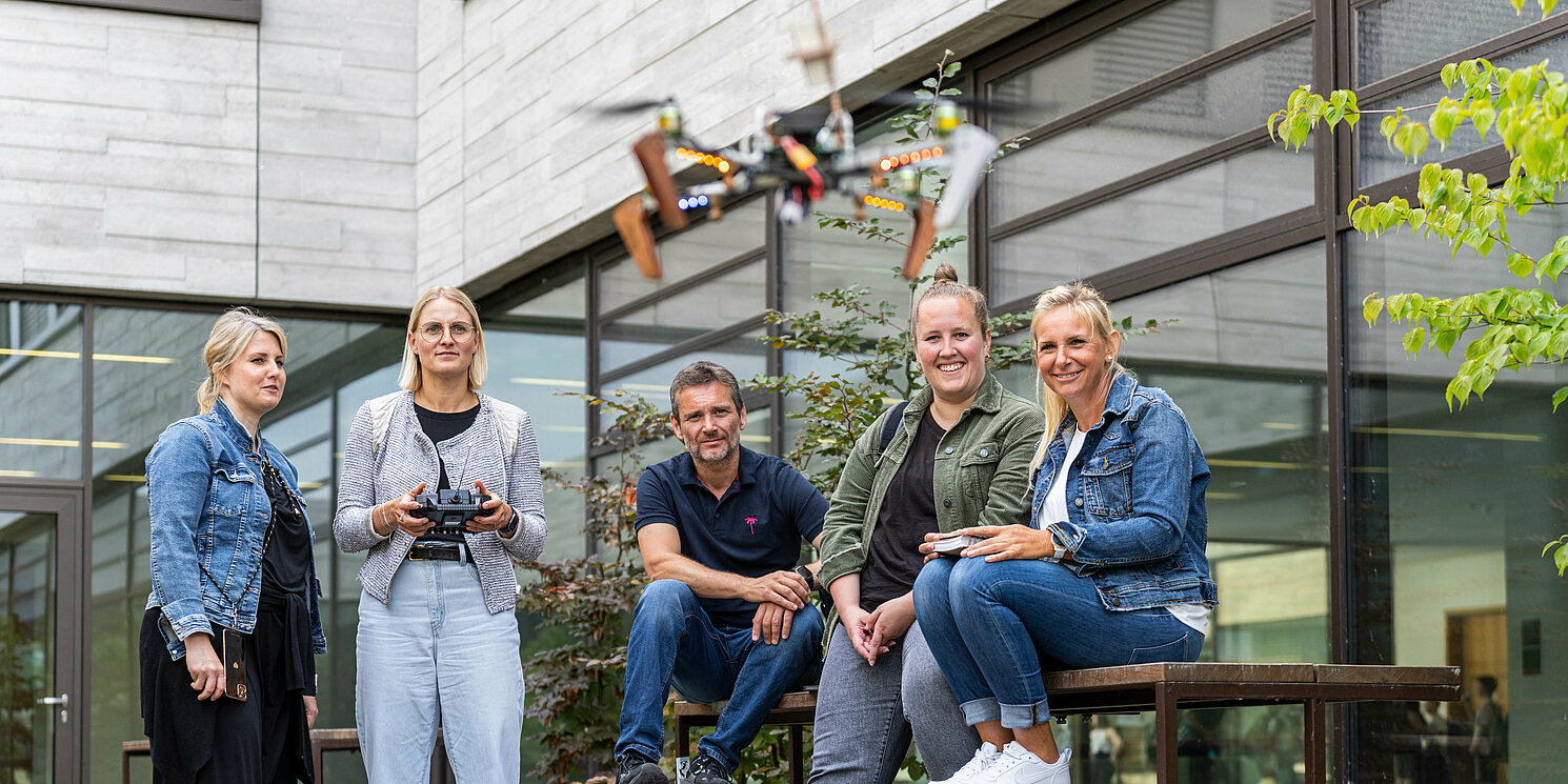 Studierende stehen in einem Innenhof und eine Studentin steuert eine fliegende Drohne.