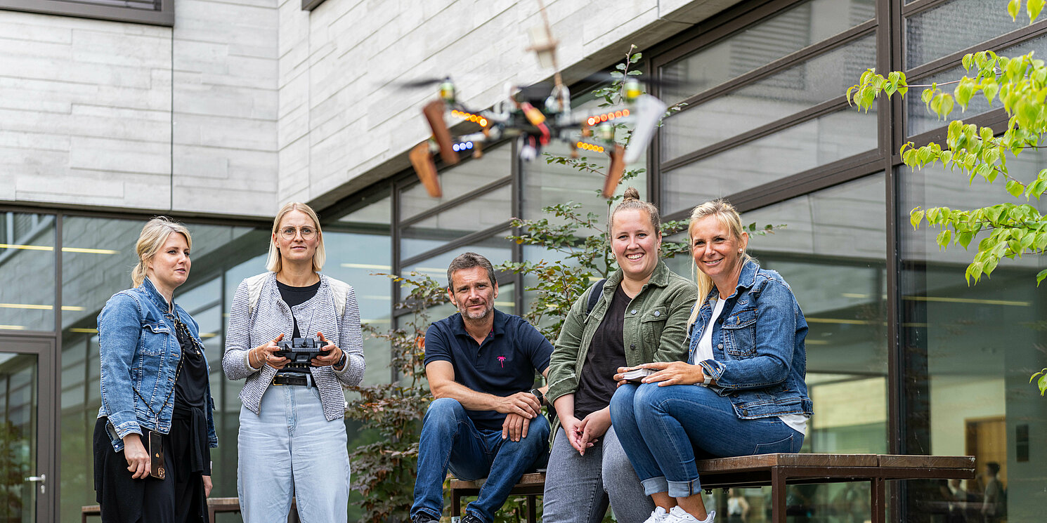 Studierende stehen in einem Innenhof und eine Studentin steuert eine fliegende Drohne.