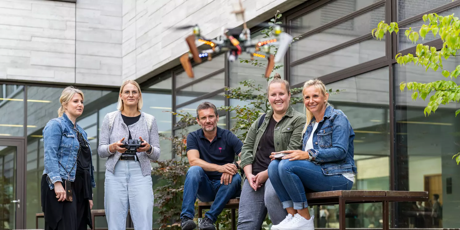 Studierende stehen in einem Innenhof und eine Studentin steuert eine fliegende Drohne.