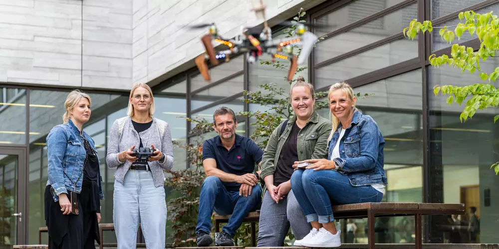 Studierende stehen in einem Innenhof und eine Studentin steuert eine fliegende Drohne.