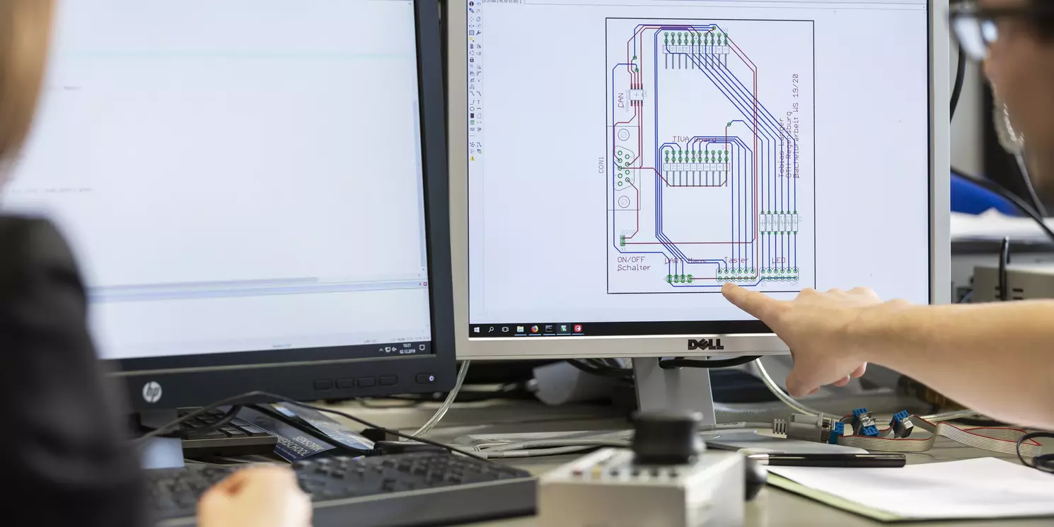 Zwei Studierende besprechen einen Platinenplan am PC.