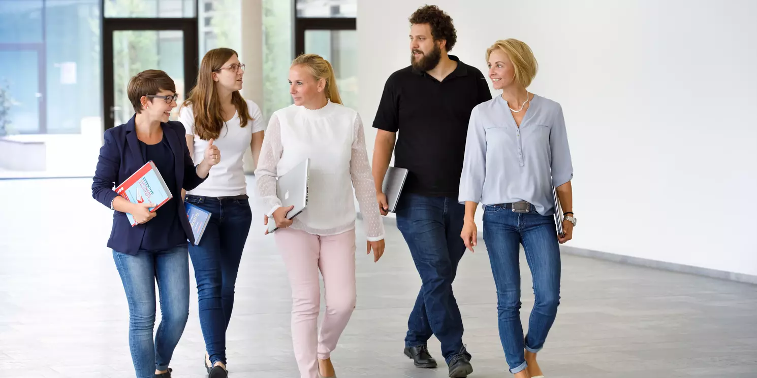 Hochschulzertifikat Business Process Manager:in berufsbegleitend absolvieren Fünf Personen gehen in einer Gruppe durch das Informatik-Foyer