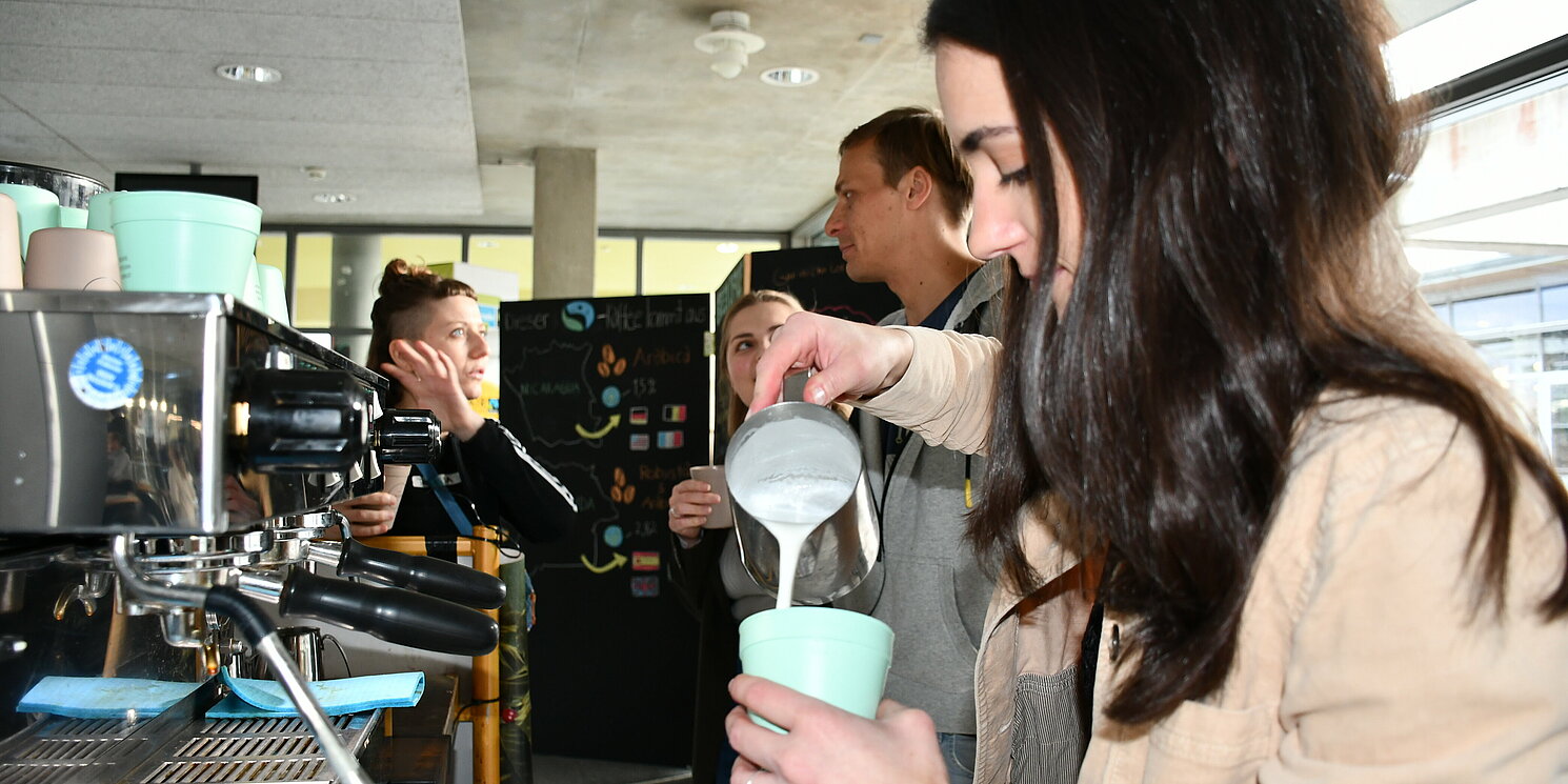 Eine Frau gießt Milch in einen Kaffeebecher.
