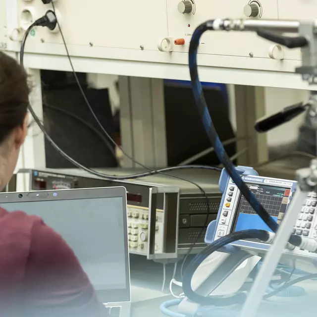 Eine Frau mit Pferdeschwanz sitzt im Labor Hochfrequenztechnik vor diversen technischen Geräten.