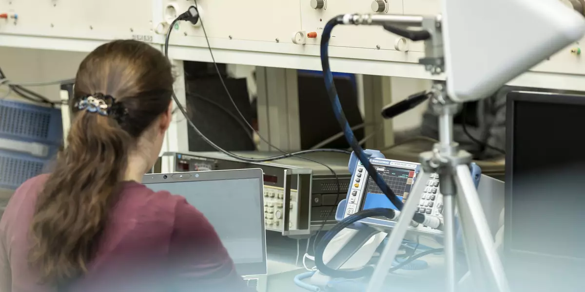 Eine Frau mit Pferdeschwanz sitzt im Labor Hochfrequenztechnik vor diversen technischen Geräten.