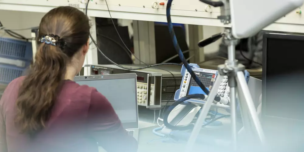 Eine Frau mit Pferdeschwanz sitzt im Labor Hochfrequenztechnik vor diversen technischen Geräten.