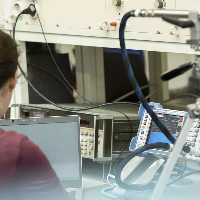 Eine Frau mit Pferdeschwanz sitzt im Labor Hochfrequenztechnik vor diversen technischen Geräten.