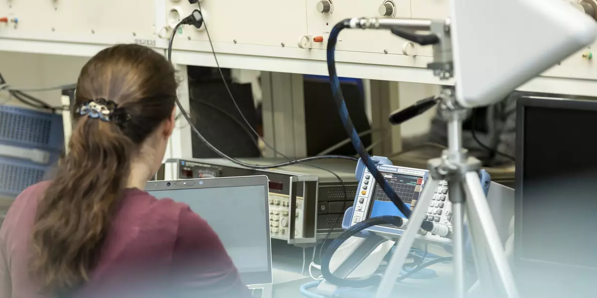 Eine Frau mit Pferdeschwanz sitzt im Labor Hochfrequenztechnik vor diversen technischen Geräten.
