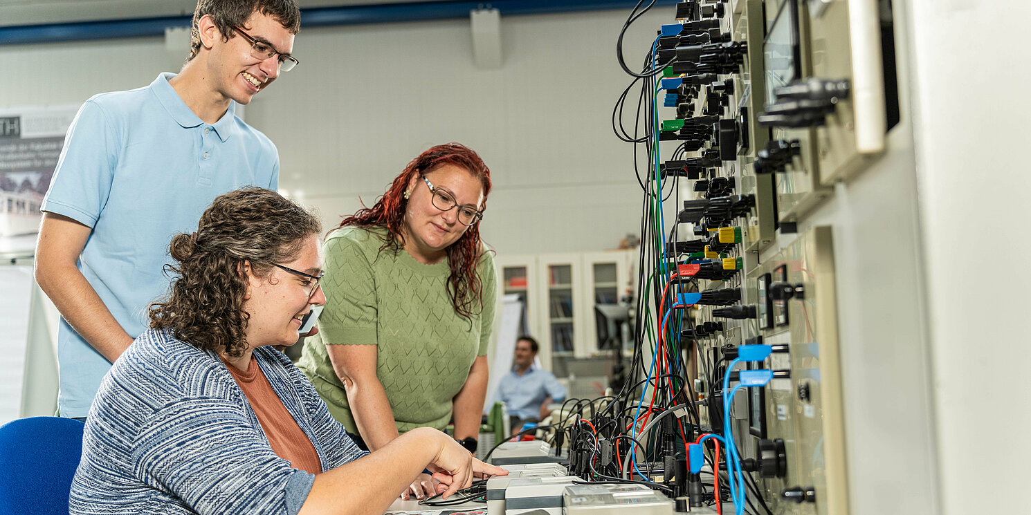 Drei Studierende arbeiten in einem Labor an einem elektronischen Schaltkasten.