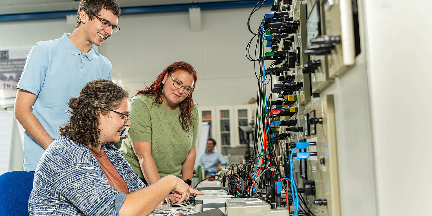 Drei Studierende arbeiten in einem Labor an einem elektronischen Schaltkasten.
