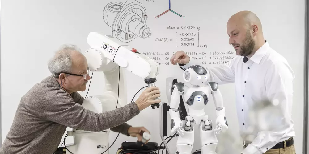 Das Bild zeigt zwei Wissenschaftler, einen jüngeren und einen älteren, die den Greifer eines 6-Achsen-Roboters für einen Zugversuch mit magneto-aktiven Polymeren wechseln.