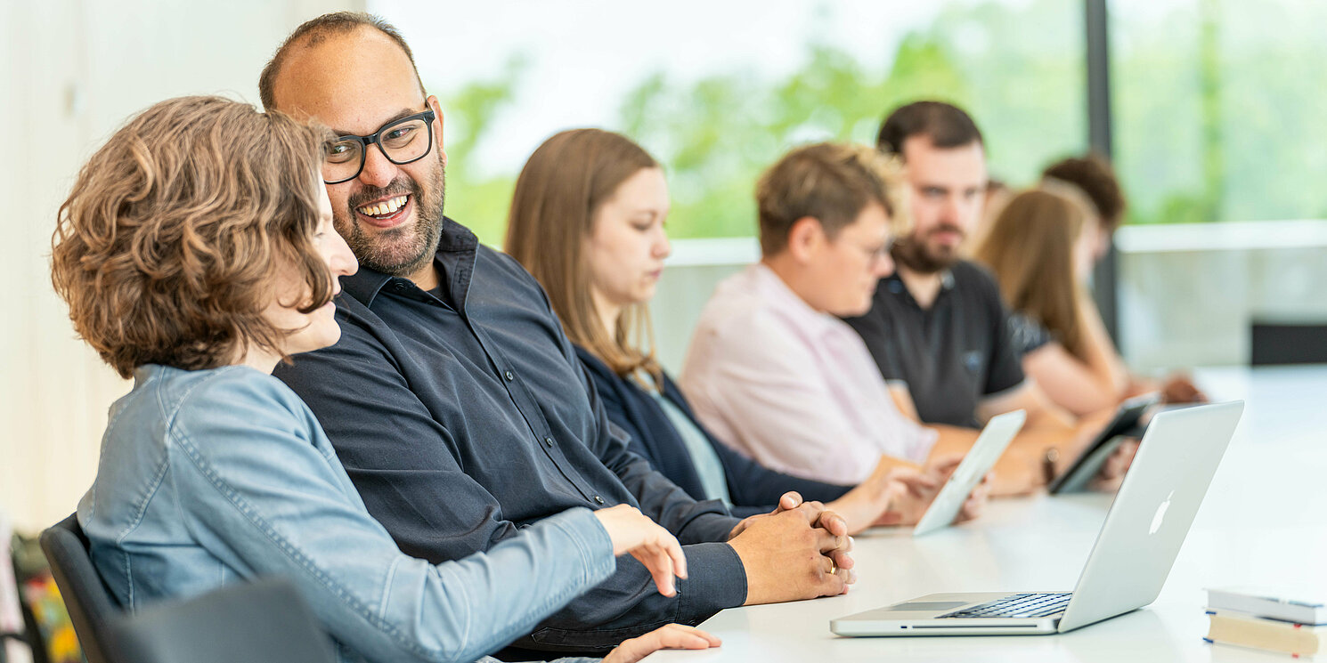 Was sagt der Studiengangleiter über den berufsbegleitenden Master Business Administration (Sie werden auf YouTube weitergeleitet) Studierende lernen und unterhalten sich in einem Seminarraum.