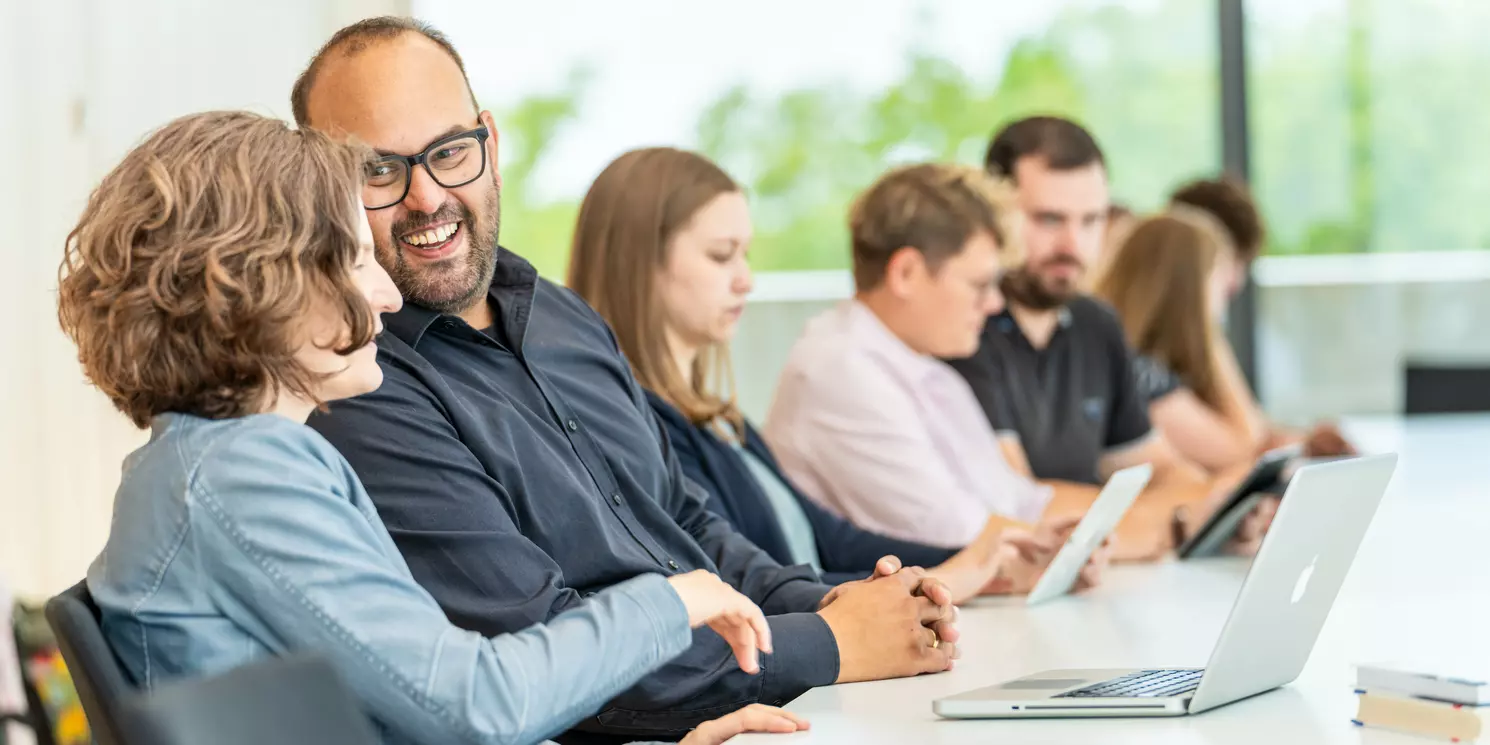 Leitung und Kommunikationsmanagement berufsbegleitend studieren Studierende lernen und unterhalten sich in einem Seminarraum.