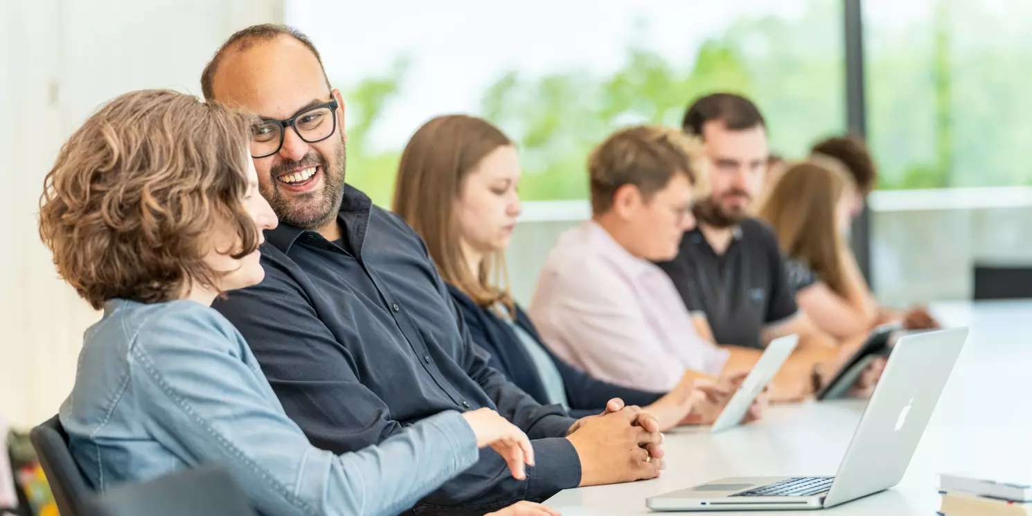 Leitung und Kommunikationsmanagement berufsbegleitend studieren Studierende lernen und unterhalten sich in einem Seminarraum.