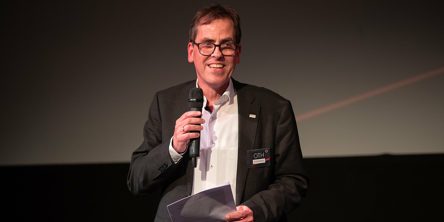 Ein Mann hält ein Mikrofon und einen Zettel in den Händen.